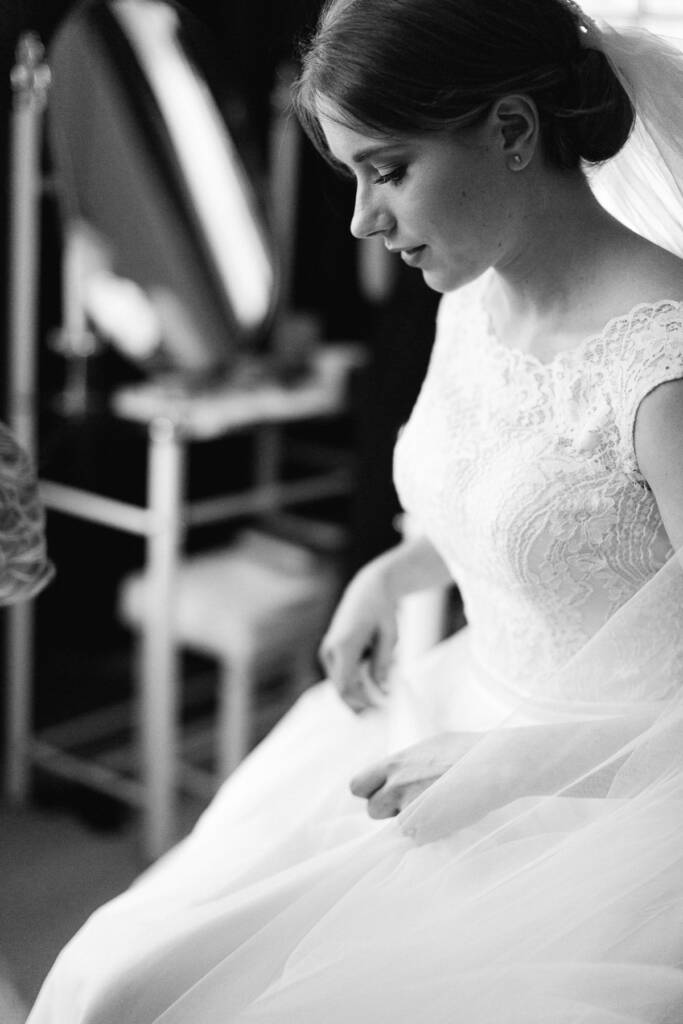 Sue sits in her veil and tulle gown, looking down during bridal preparations.