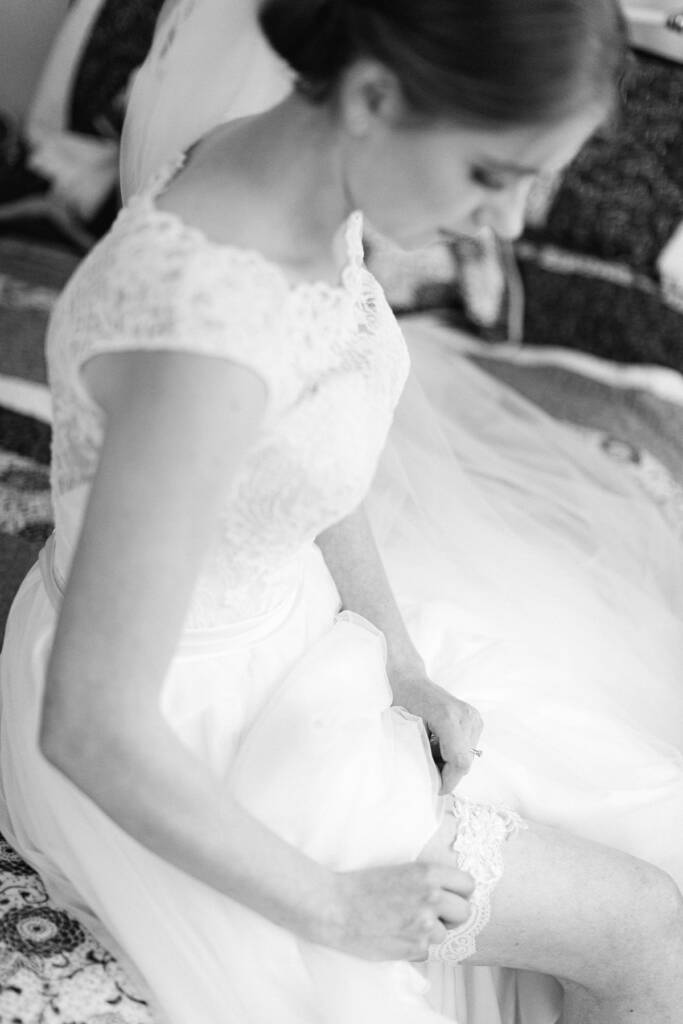From above, Sue seated on a quilt lifts the tulle to show a lace garter.