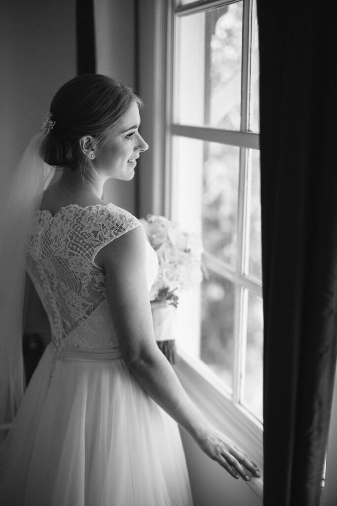 Profile of Sue smiling at the sash window, hair comb, veil and white rose bouquet.