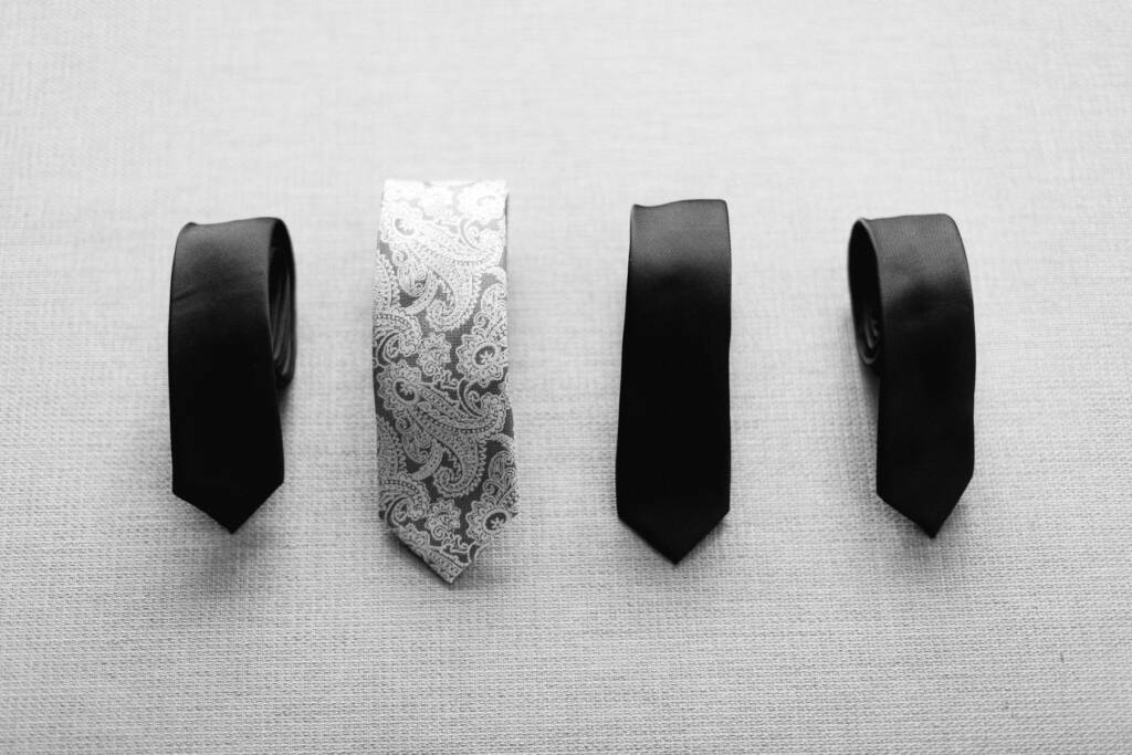 Flat lay of four ties on linen, three plain black and one silver paisley.