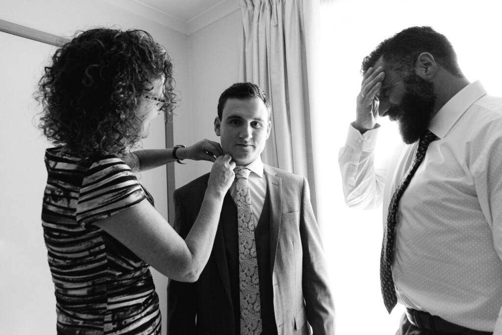 An adult adjusts Chris's collar as a bearded man stands beside him at home in Mount Waverley.
