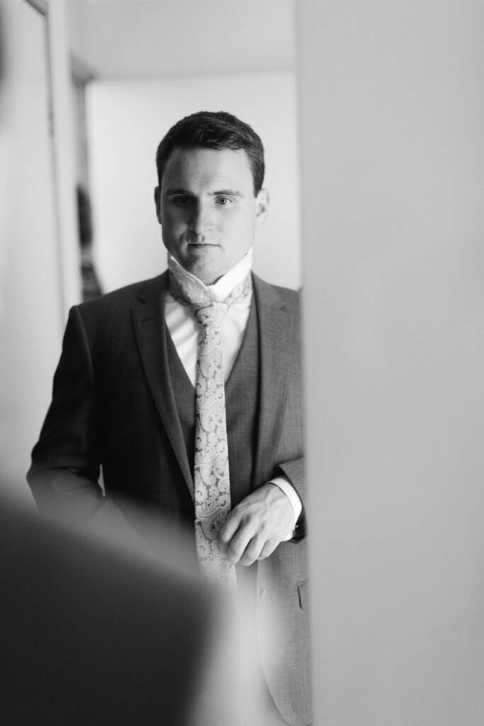 Chris looks into a mirror with his collar raised and paisley tie loosened at his Mount Waverley home.