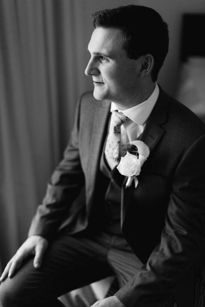 Black and white of Chris seated in profile by a curtain, hands on his knees.