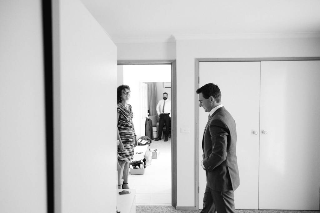 Chris stands in his wedding suit as adults gather in a doorway at his Mount Waverley home.