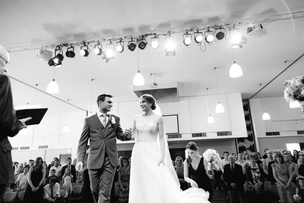 Sue and Chris hold hands at Syndal Baptist Church as an attendant arranges her train.