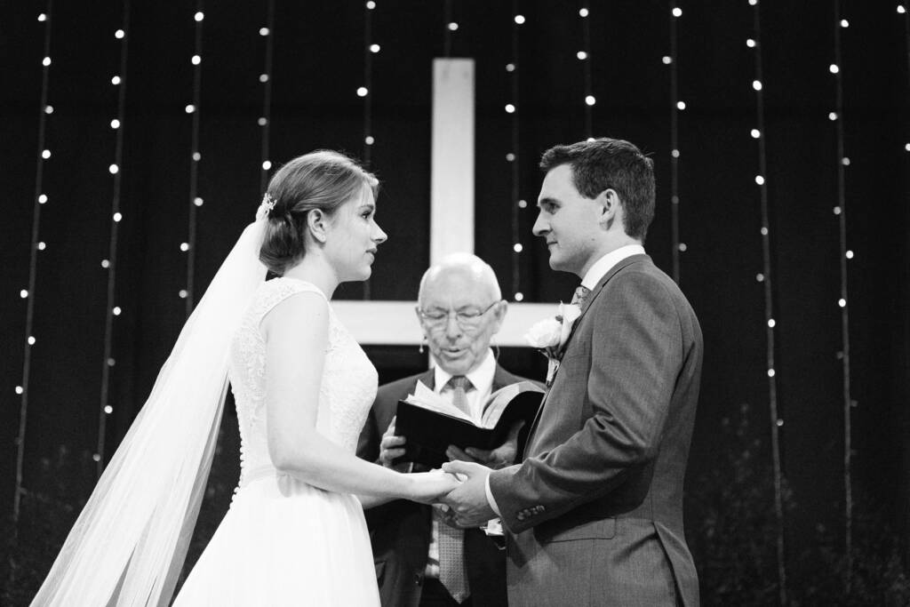 Sue and Chris hold hands before the cross as the officiant reads at Syndal Baptist Church.