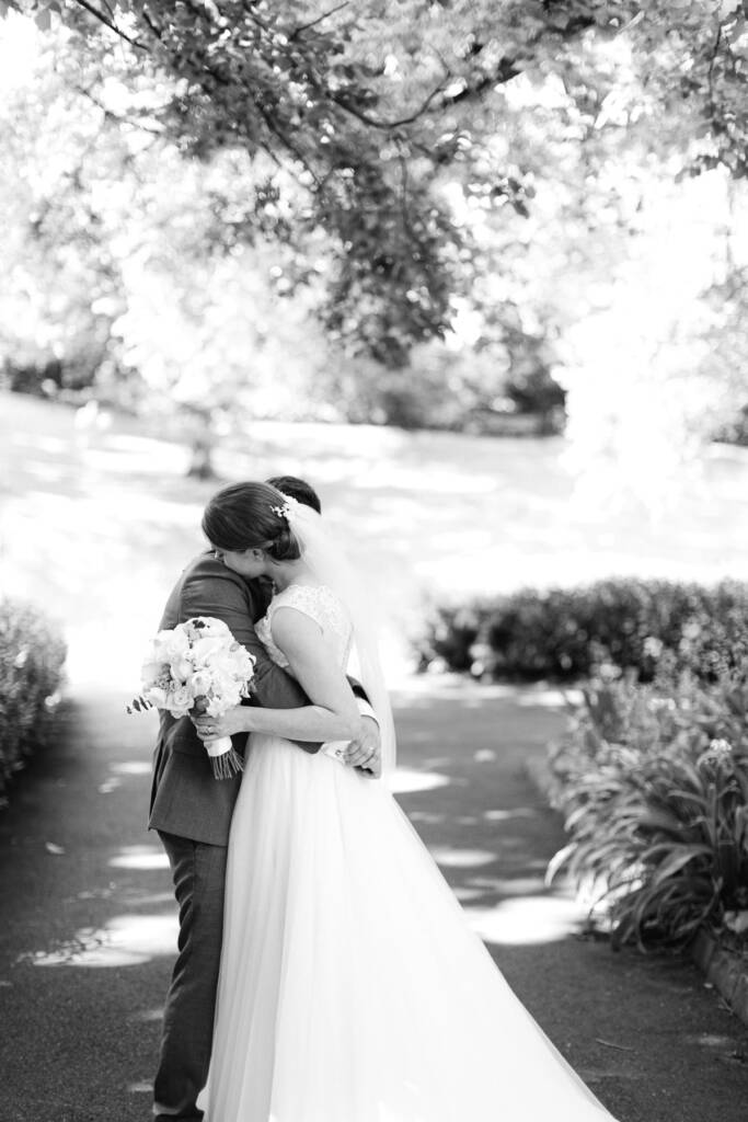 Sue and Chris embrace on a path at Canterbury Gardens, her bouquet behind his back.