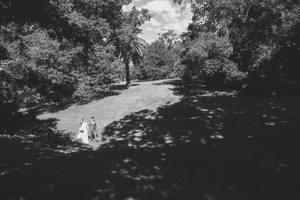 Sue and Chris hold hands across the broad lawn and trees of Canterbury Gardens.