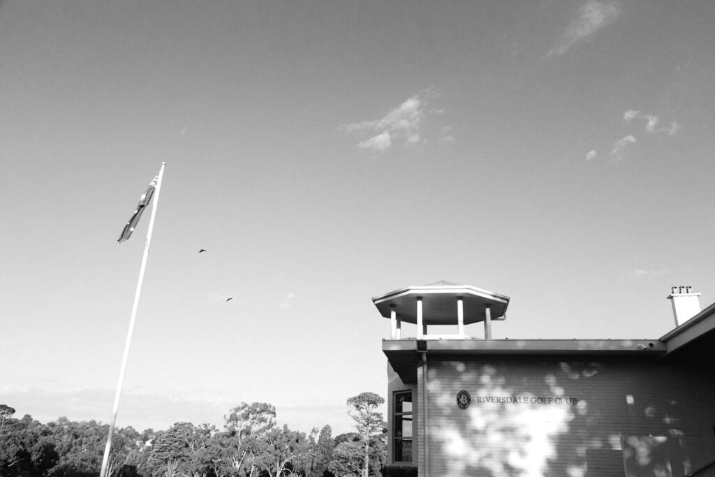 The Riversdale Golf Club clubhouse cupola and lettered wall beneath a flagpole and a big sky.