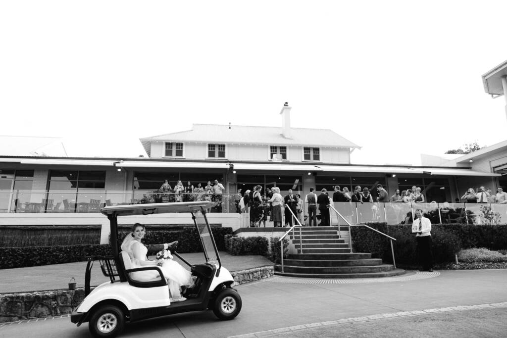 Sue arrives at the Riversdale Golf Club clubhouse by golf cart as guests line the terrace above.