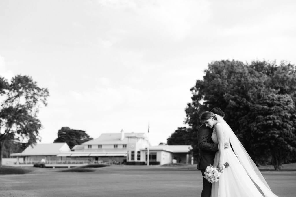 Sue rests her head on Chris's shoulder on a Riversdale Golf Club fairway with the clubhouse behind them.