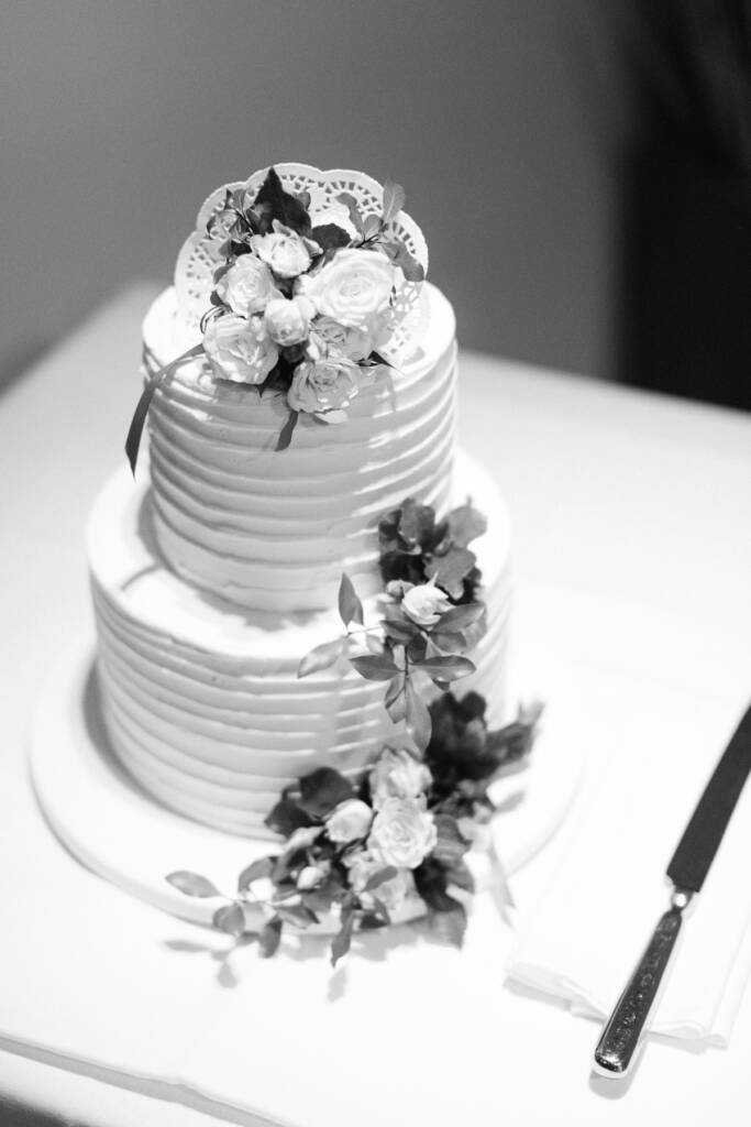 A two-tier wedding cake with ridged icing, roses, greenery and a knife at Riversdale Golf Club.