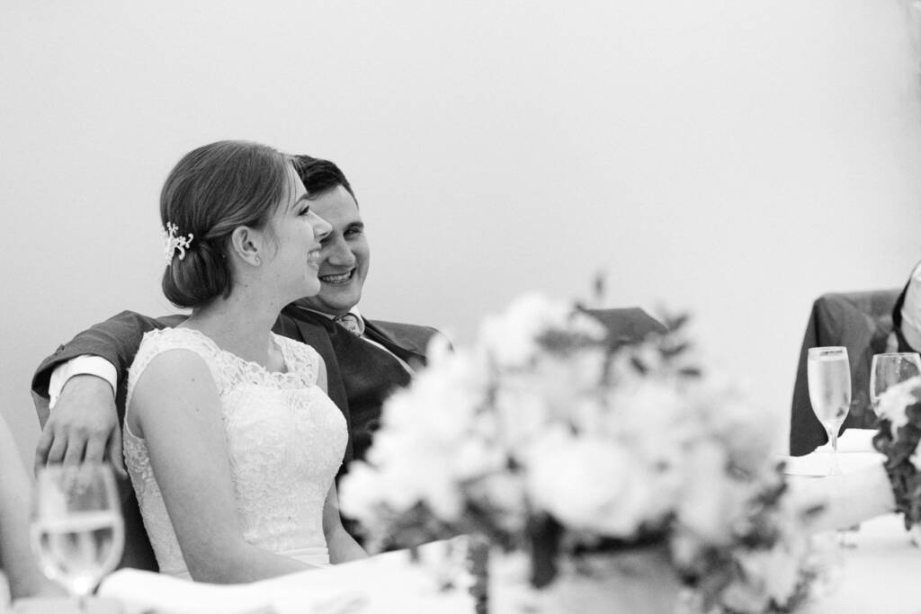 Sue and Chris smile at the Riversdale bridal table with flowers and flutes in the foreground.