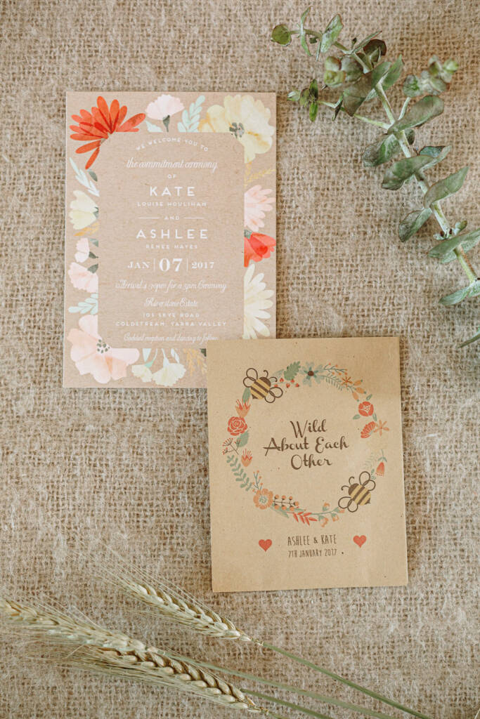 Ashlee and Kate's Riverstone Estate commitment-ceremony invitation and illustrated card lie on hessian with eucalyptus and grain stalks.
