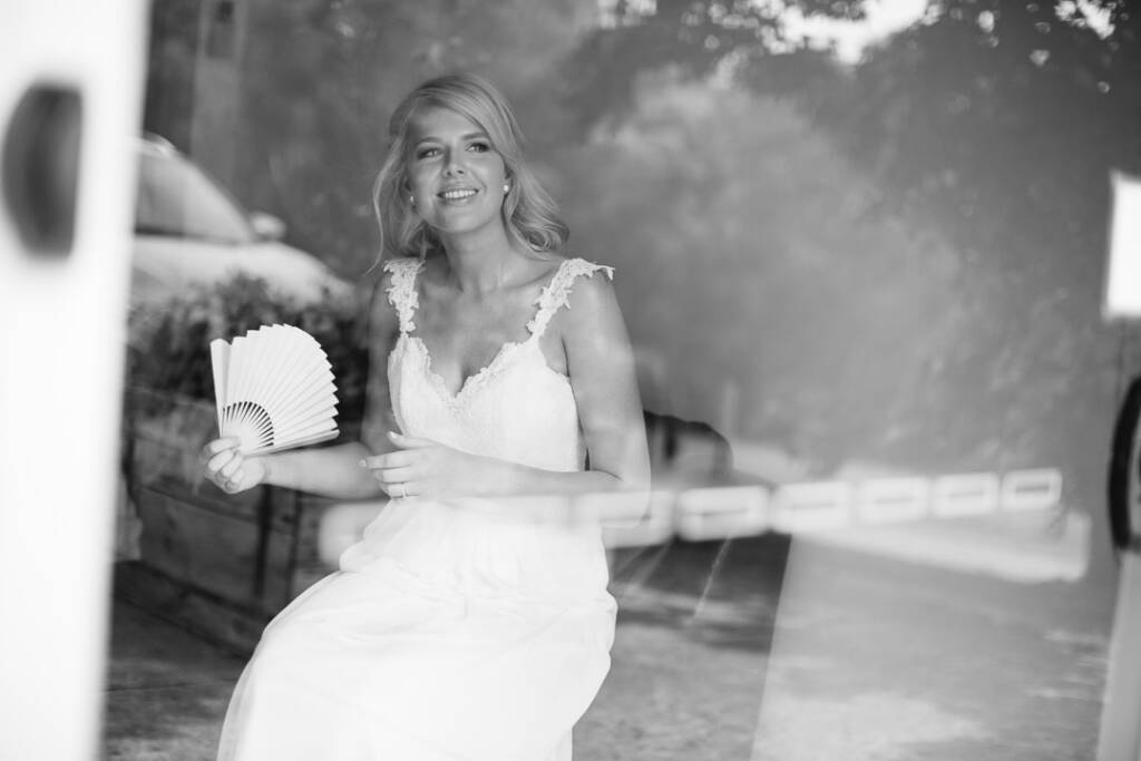 Kate holds a paper fan, photographed through reflective glass at her Chum Creek Airbnb in black and white.