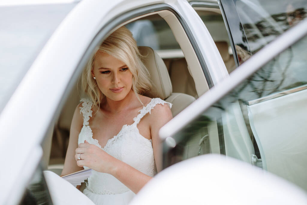 Kate sits inside a white car with the door open, holding a paper fan.