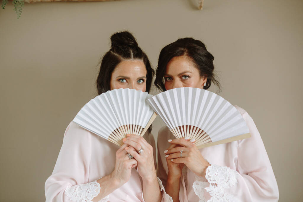 Ashlee and a companion pose with open paper fans covering the lower halves of their faces.