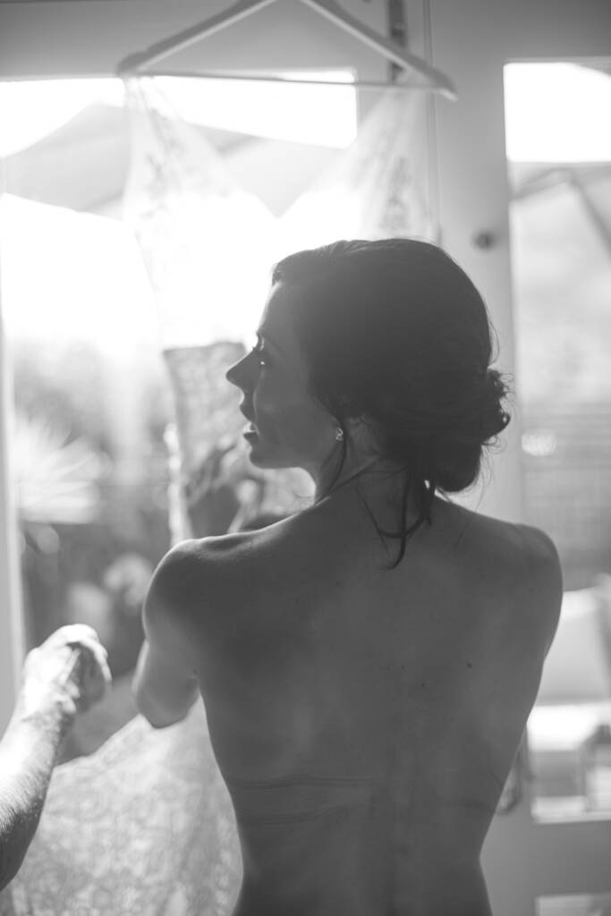 Black-and-white photo of Ashlee getting ready beside her hanging gown.