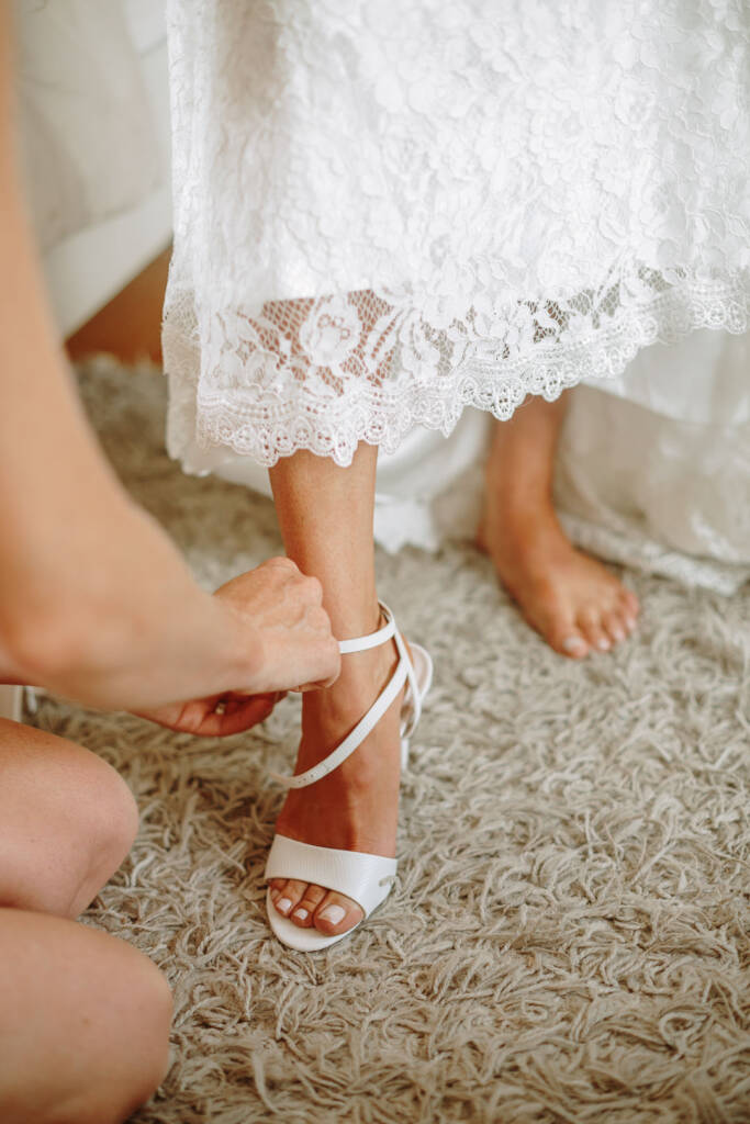 A helper fastens Ashlee's ankle-strap heel beneath the scalloped lace hem of her gown.
