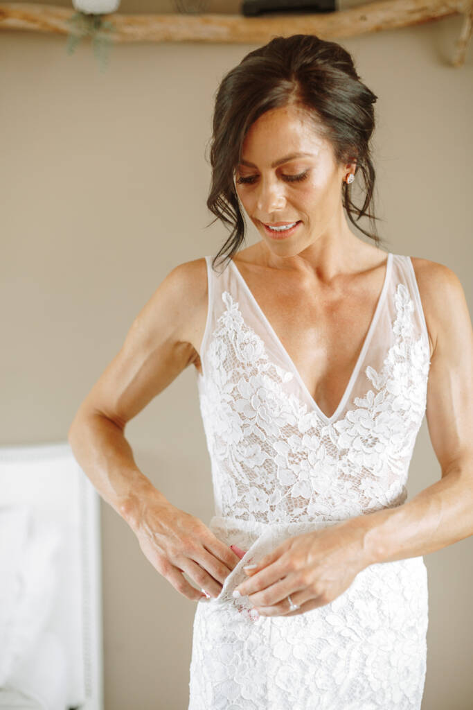Ashlee looks down with her hands at the waist of her lace gown.