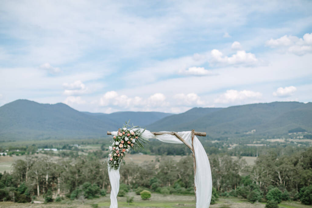 A timber arbour with white draping and peach flowers overlooks the Yarra Valley at Riverstone Estate.