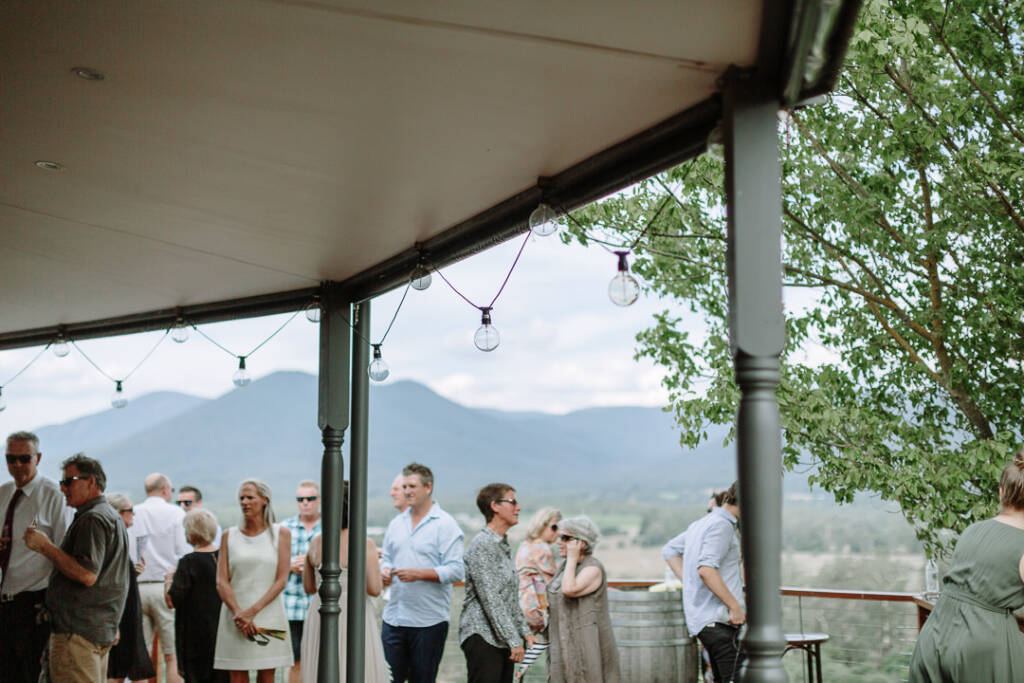 Guests gather on Riverstone's covered verandah with wine barrels and valley views.