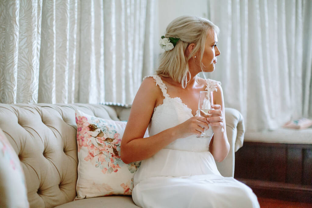 Kate sits with a flute on a cream sofa beside the window at Riverstone.