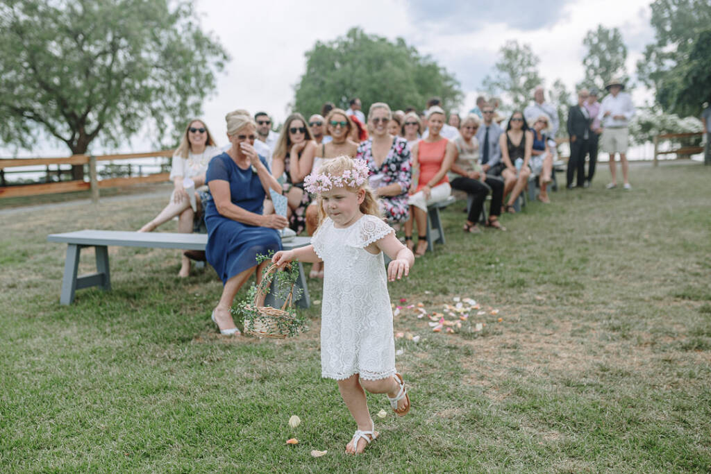 A flower girl carries her basket along the petal-strewn lawn aisle at Riverstone.