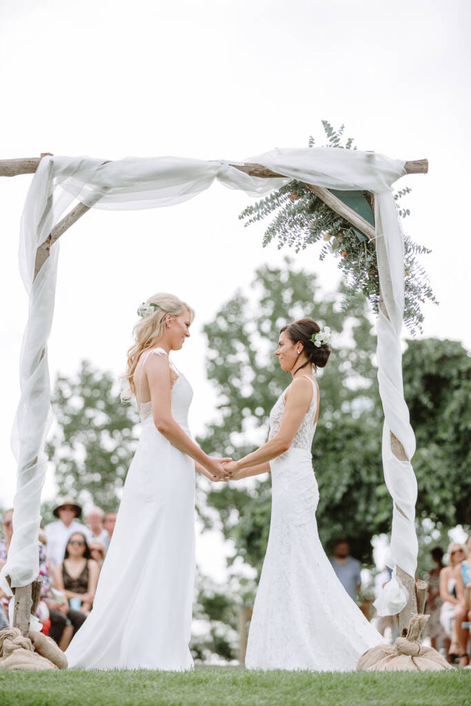 Ashlee and Kate face each other beneath the white-draped arbour at Riverstone Estate.