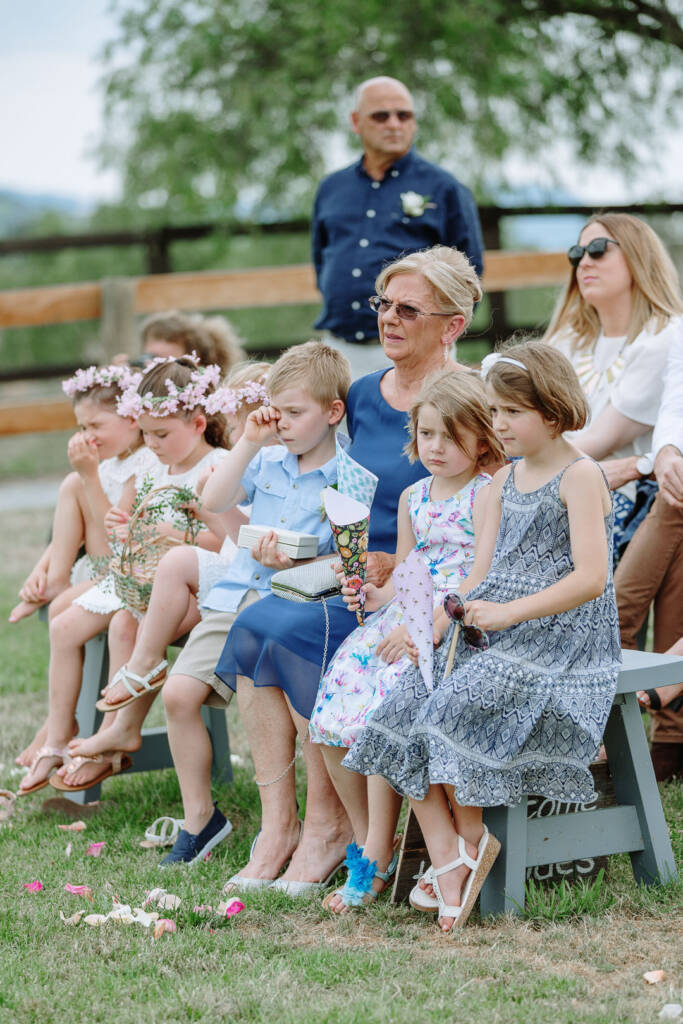 Children and guests sit along a bench beside the lawn aisle at Riverstone.
