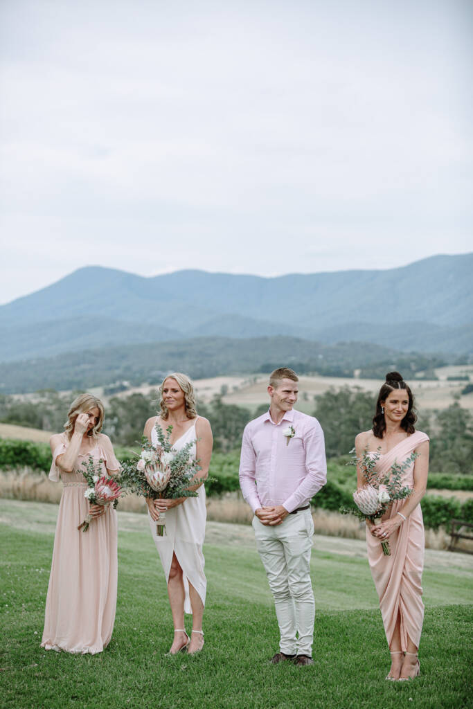 Attendants in pink and cream stand on the lawn overlooking the vines at Riverstone.