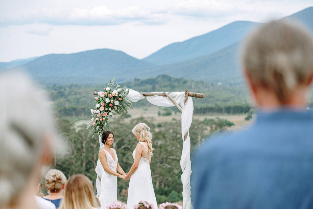 Guests watch Ashlee and Kate holding hands beneath the arbour above Riverstone Estate's vineyard.