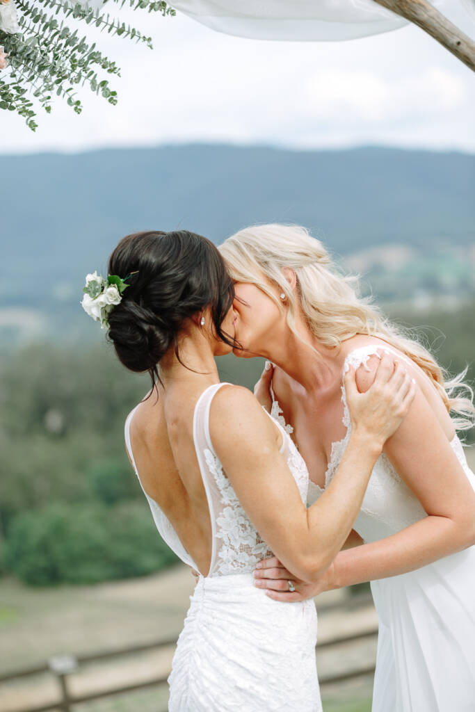 Ashlee and Kate kiss beneath the white-draped arbour at Riverstone Estate.