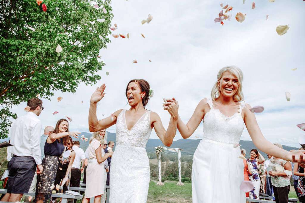 Ashlee and Kate walk hand in hand through a petal shower at Riverstone.