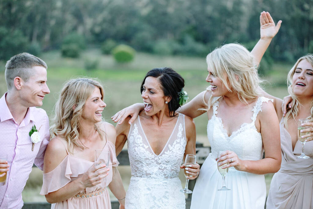 Ashlee and Kate laugh with their attendants, holding drinks after the ceremony.