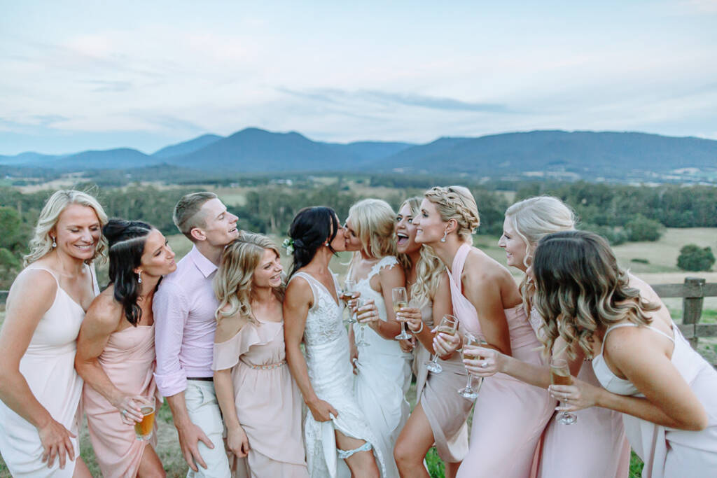 Ashlee and Kate kiss among their attendants during a group portrait at Riverstone.