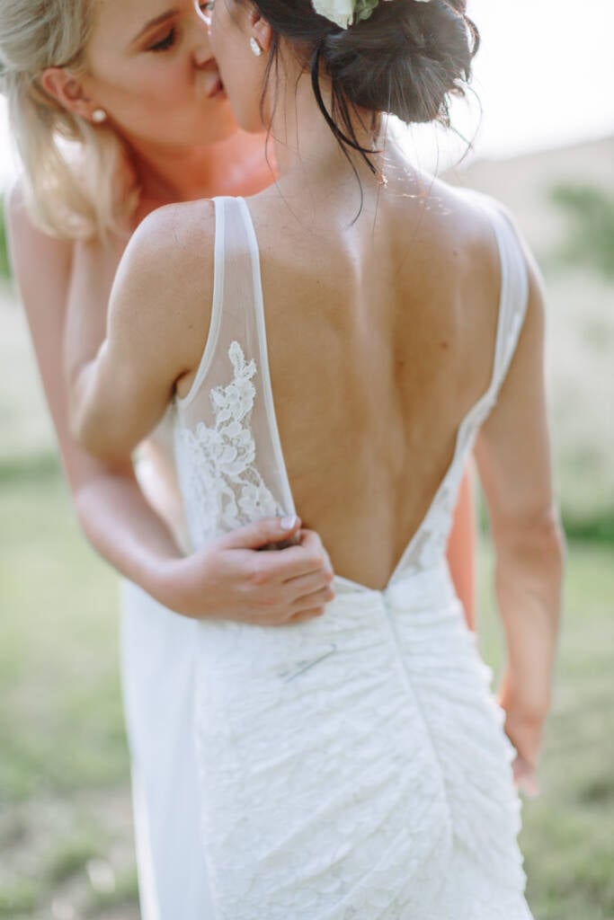 Close-up of Kate kissing Ashlee, with a hand around the lace back of her gown.