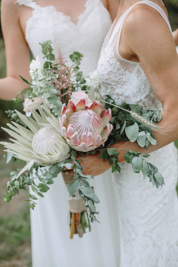The couple hold protea and eucalyptus bouquets against their lace gowns.