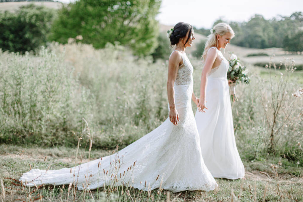 Ashlee and Kate walk hand in hand through tall grasses at Riverstone Estate.