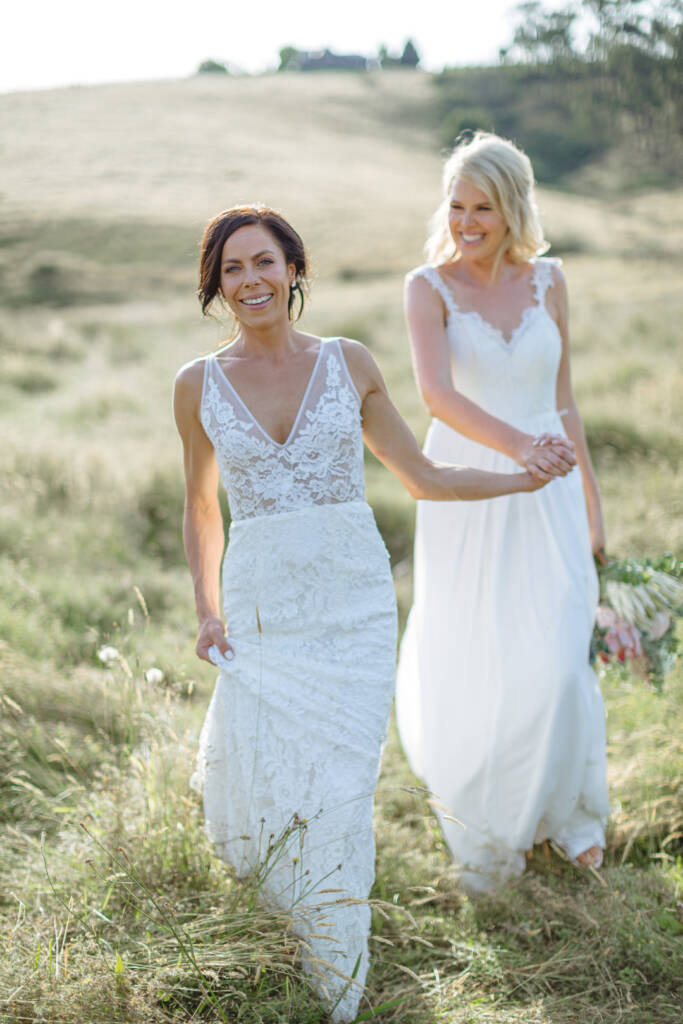 Ashlee leads Kate by the hand through the grass at Riverstone, with the homestead on the hill behind.