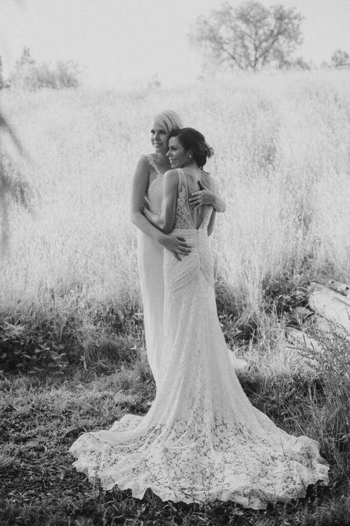 Black-and-white portrait of the couple embracing with Ashlee's lace train spread across the grass at Riverstone.