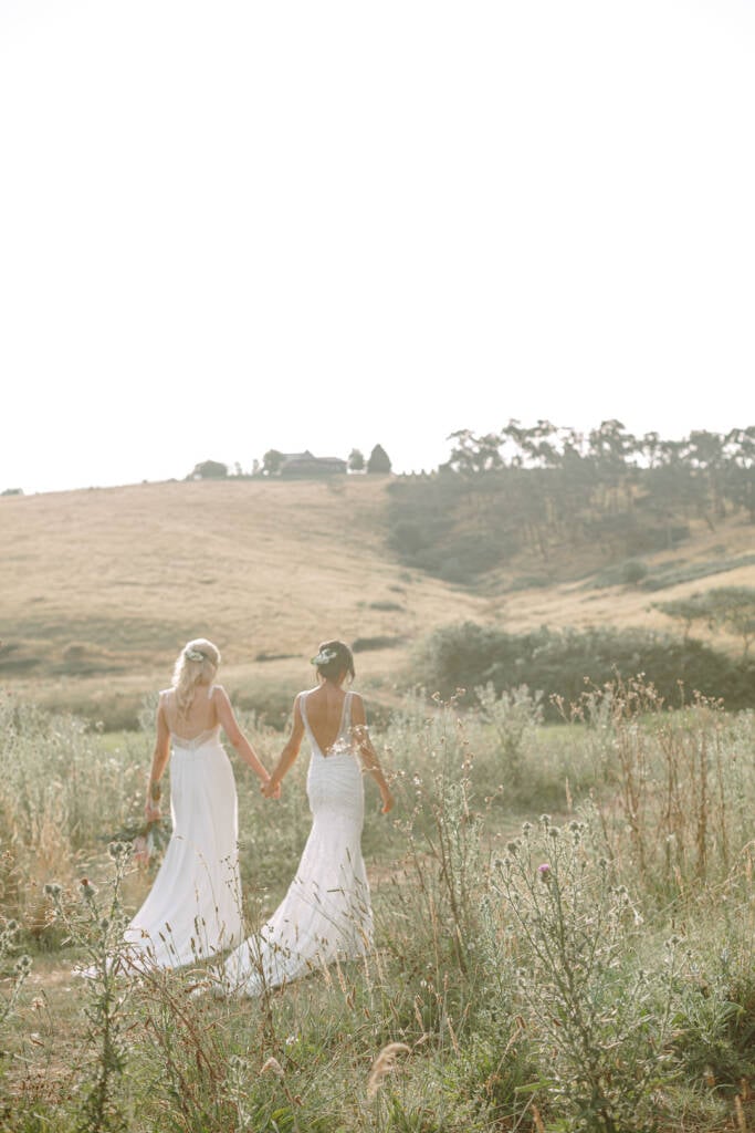 Backlit portrait of Ashlee and Kate walking through tall grasses towards the hilltop homestead at Riverstone.