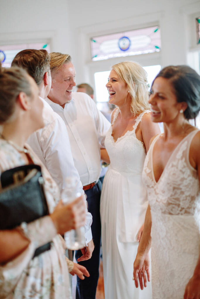 Ashlee and Kate laugh with guests beneath the leadlight windows at Riverstone Estate.