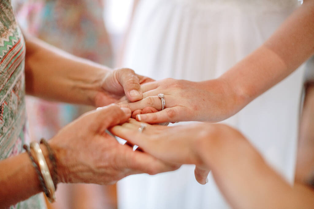 A guest holds both brides' ringed hands during the reception.
