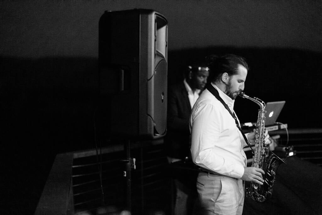 A saxophonist performs beside the DJ at Riverstone Estate in black and white.