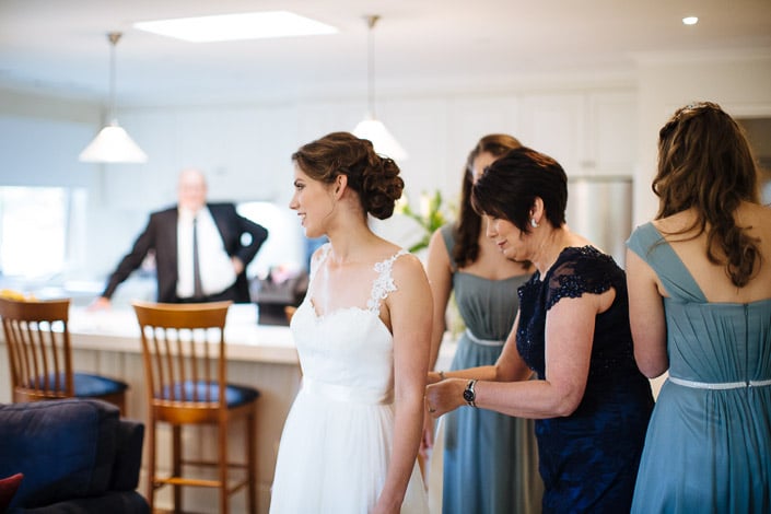 In profile, Frances smiles while the back of her lace gown is fastened before the ceremony.