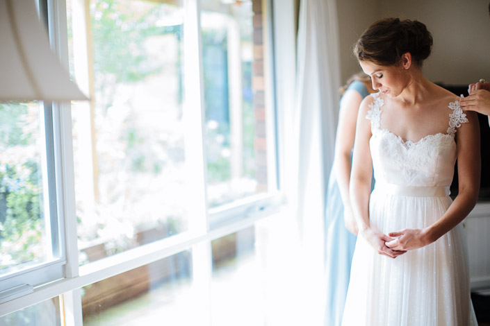 Dotted tulle catches the window light as Frances looks down at her folded hands.