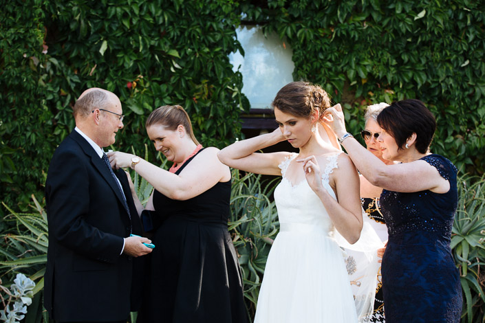 A boutonniere is pinned on at left while Frances fixes her hair against a green wall.