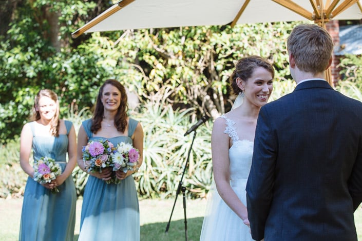 Frances laughs mid-ceremony under a market umbrella while the bridesmaids hold their dahlia posies.