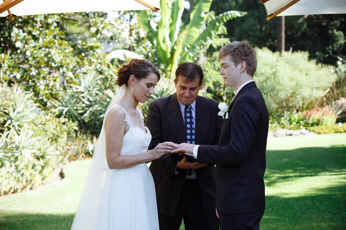The ring goes onto Tim's finger as the celebrant looks on in the garden.